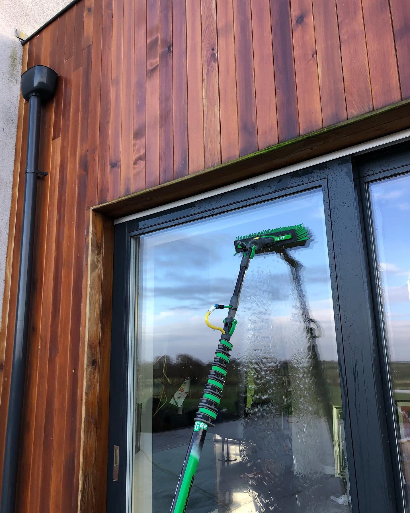 Water-fed pole and brush cleaning a window on a timber-clad house near Navan